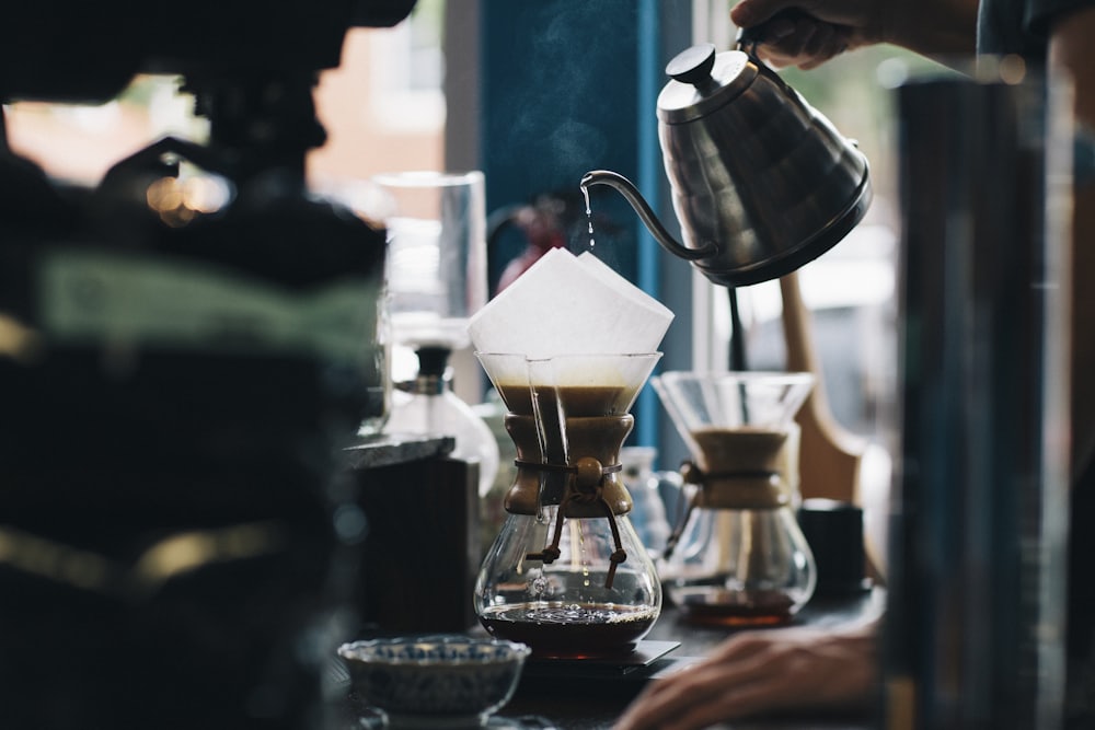 A gooseneck kettle pouring water over a paper filter in a glass brewer.